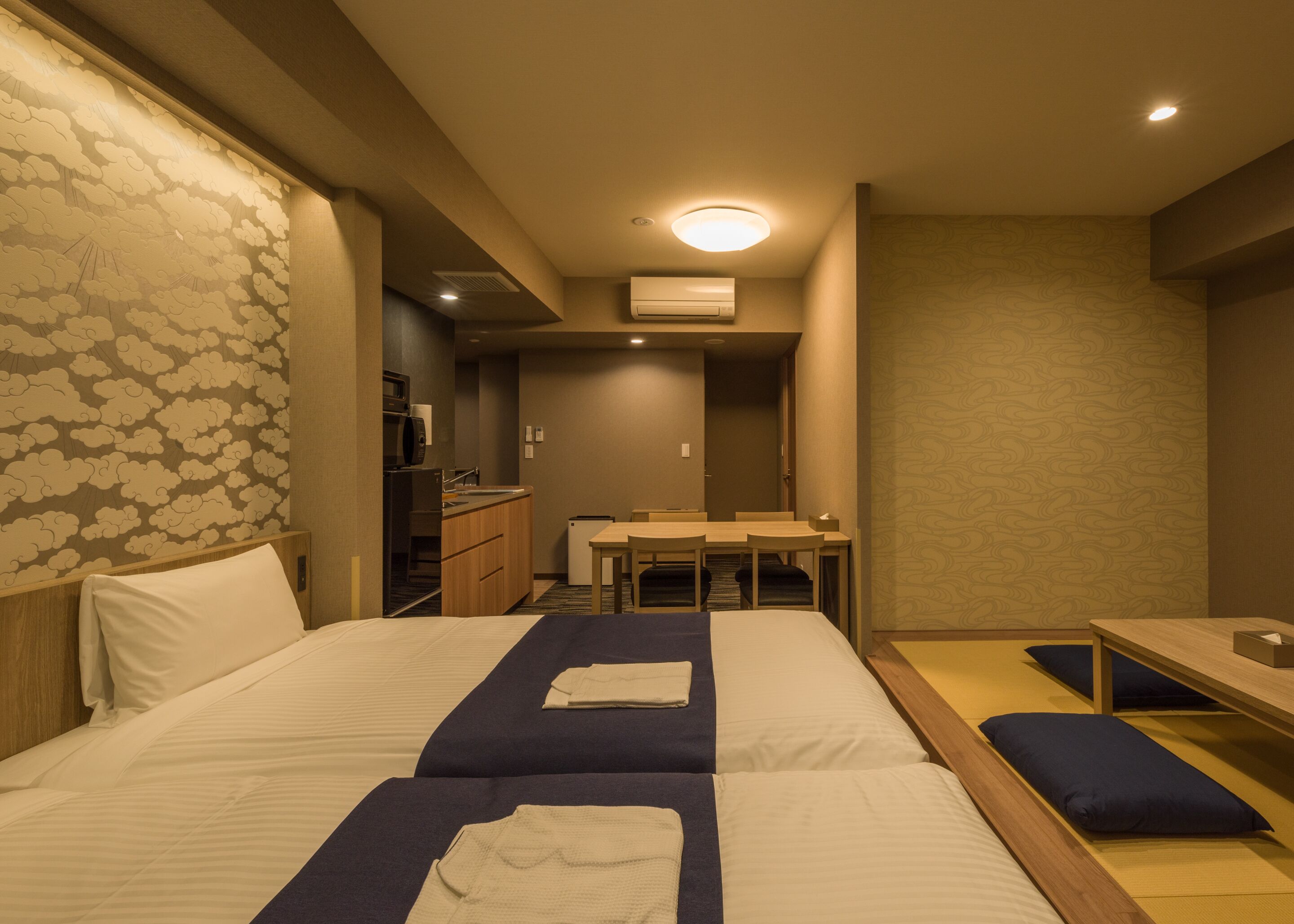 A hotel room with a bed, a desk, and a kitchenette.