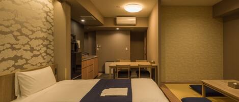 A hotel room with a bed, a desk, and a kitchenette.