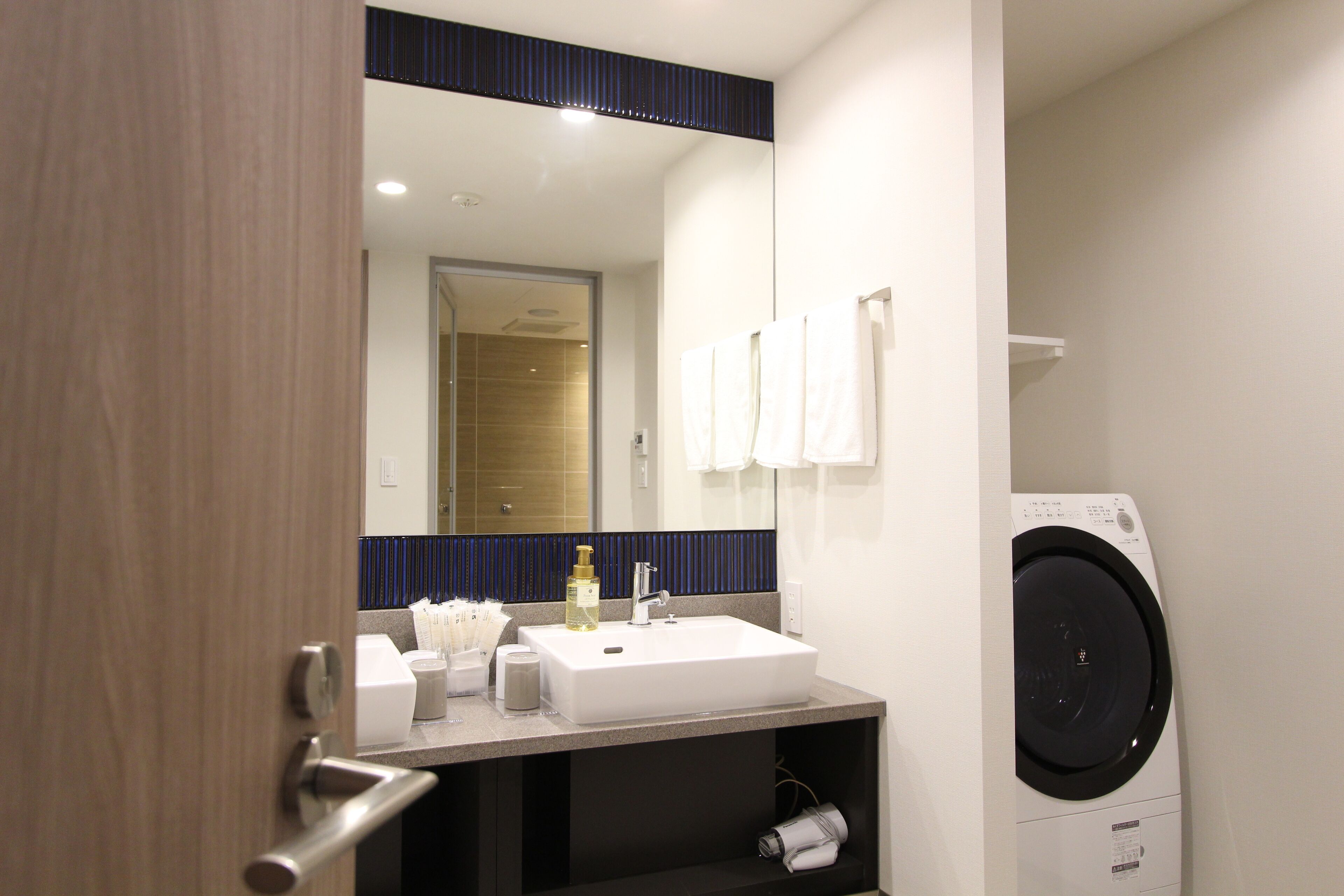 Une salle de bain moderne équipée d’un lavabo, d’un miroir, d’un porte-serviettes et d’un lave-linge.