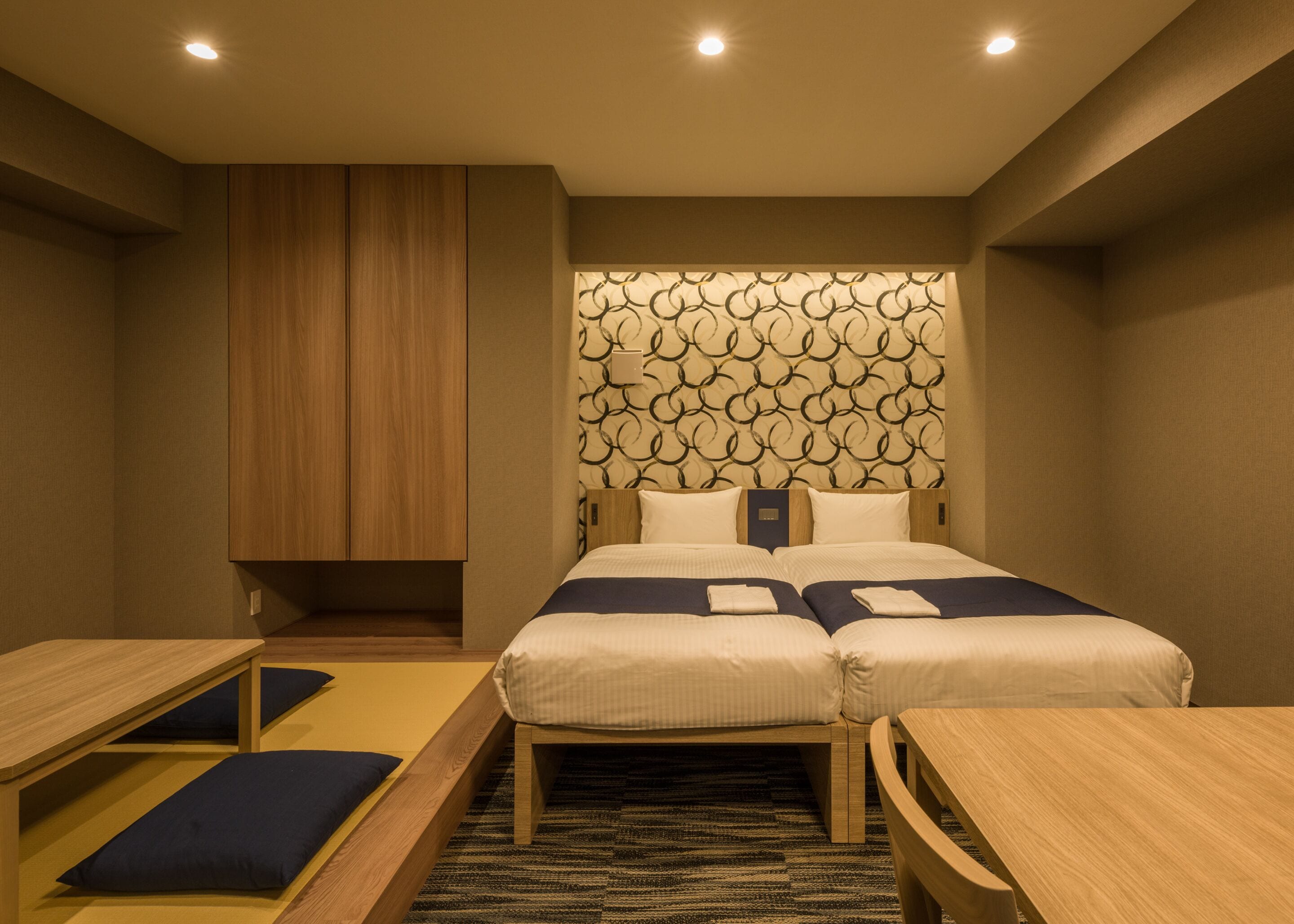 Una habitación de hotel con una cama, dos mesitas de noche, un armario de madera y un cabecero estampado.
