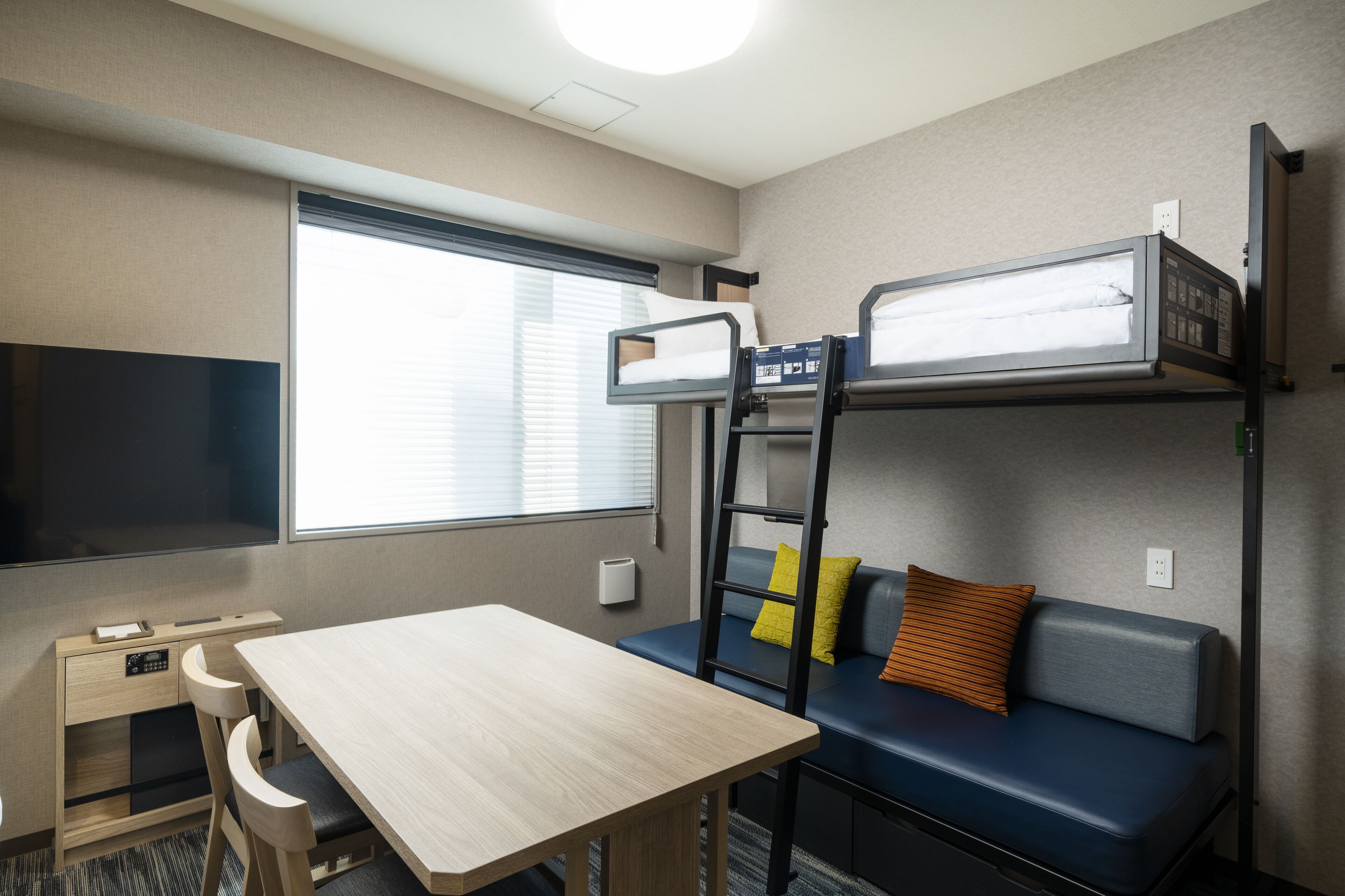 A compact hotel room with a bunk bed, a desk with a chair, a small table, and a sofa.