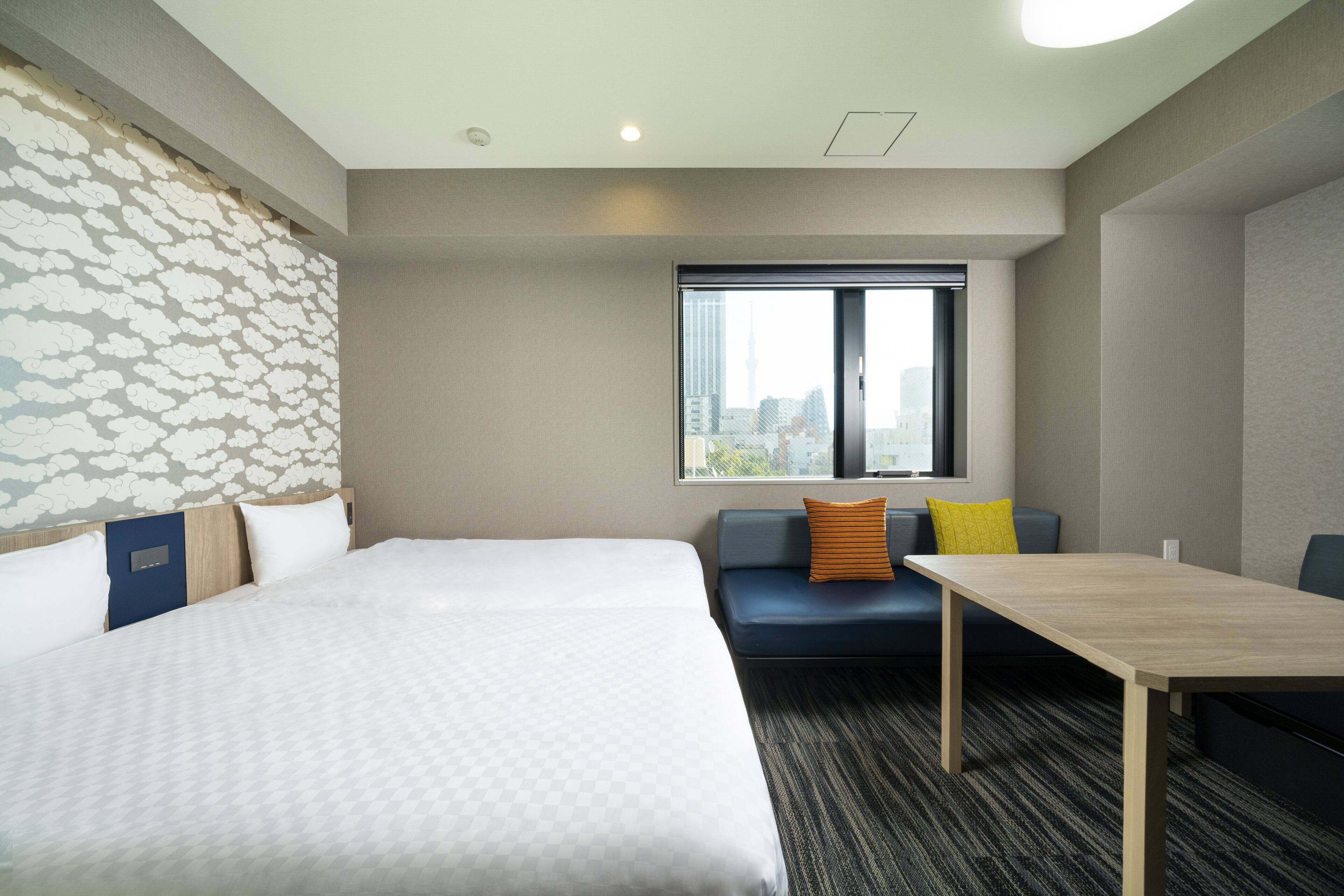 A hotel room with a large bed, a sofa, a small table, and a window with a city view.
