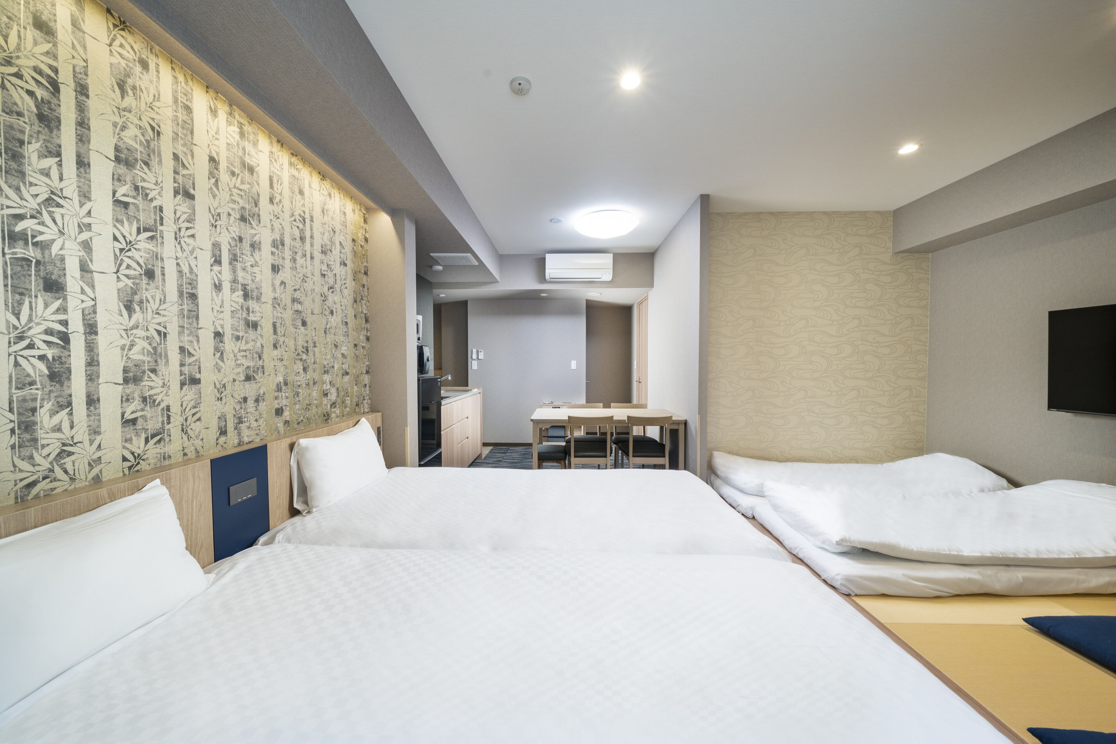 A hotel room with two beds, a desk, and a bathroom.