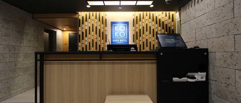 A reception desk with a wooden panel backdrop, a digital screen, and a small bench.