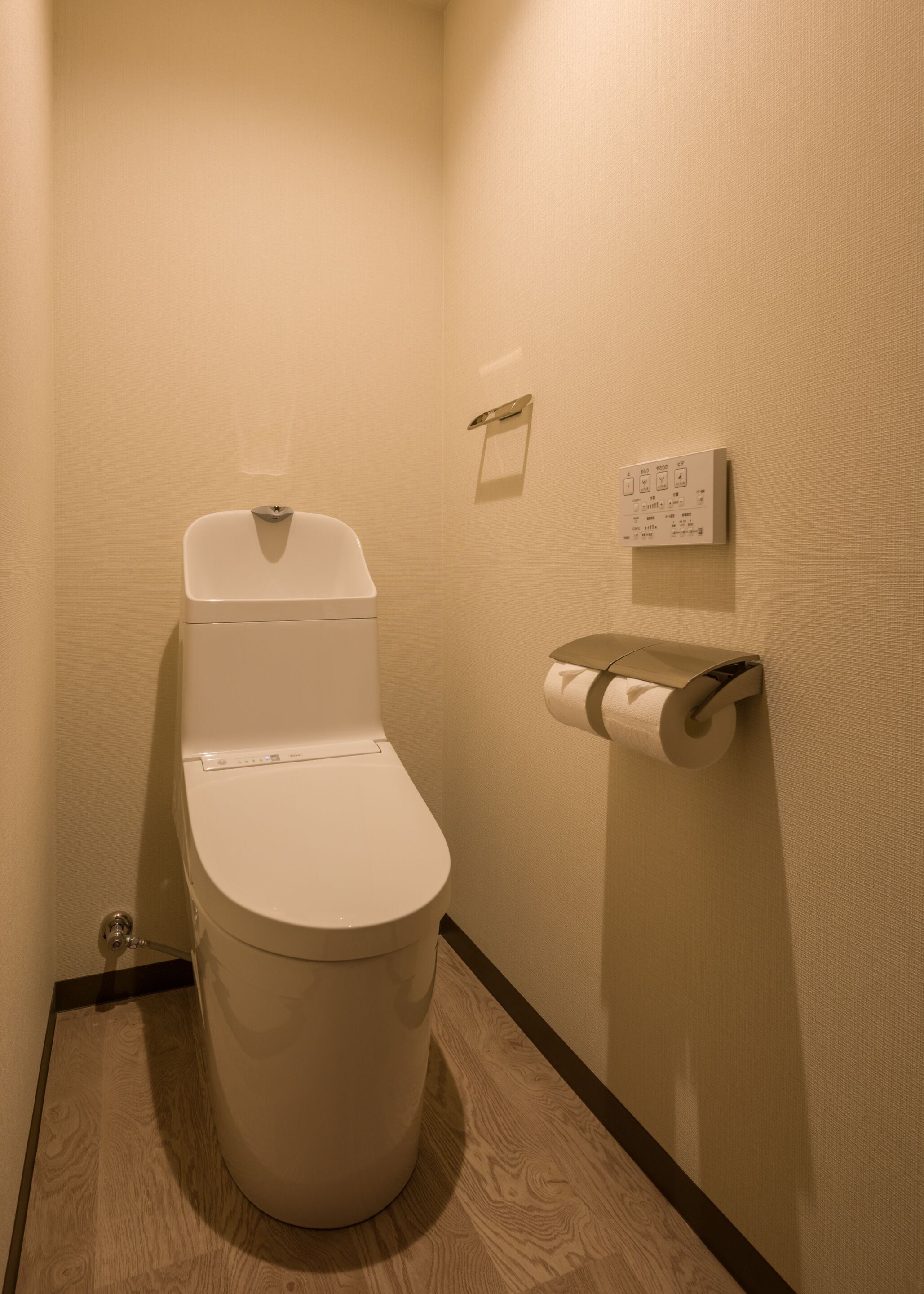 Un baño de hotel estándar con inodoro, dispensador de toallas de papel y panel de control en la pared.