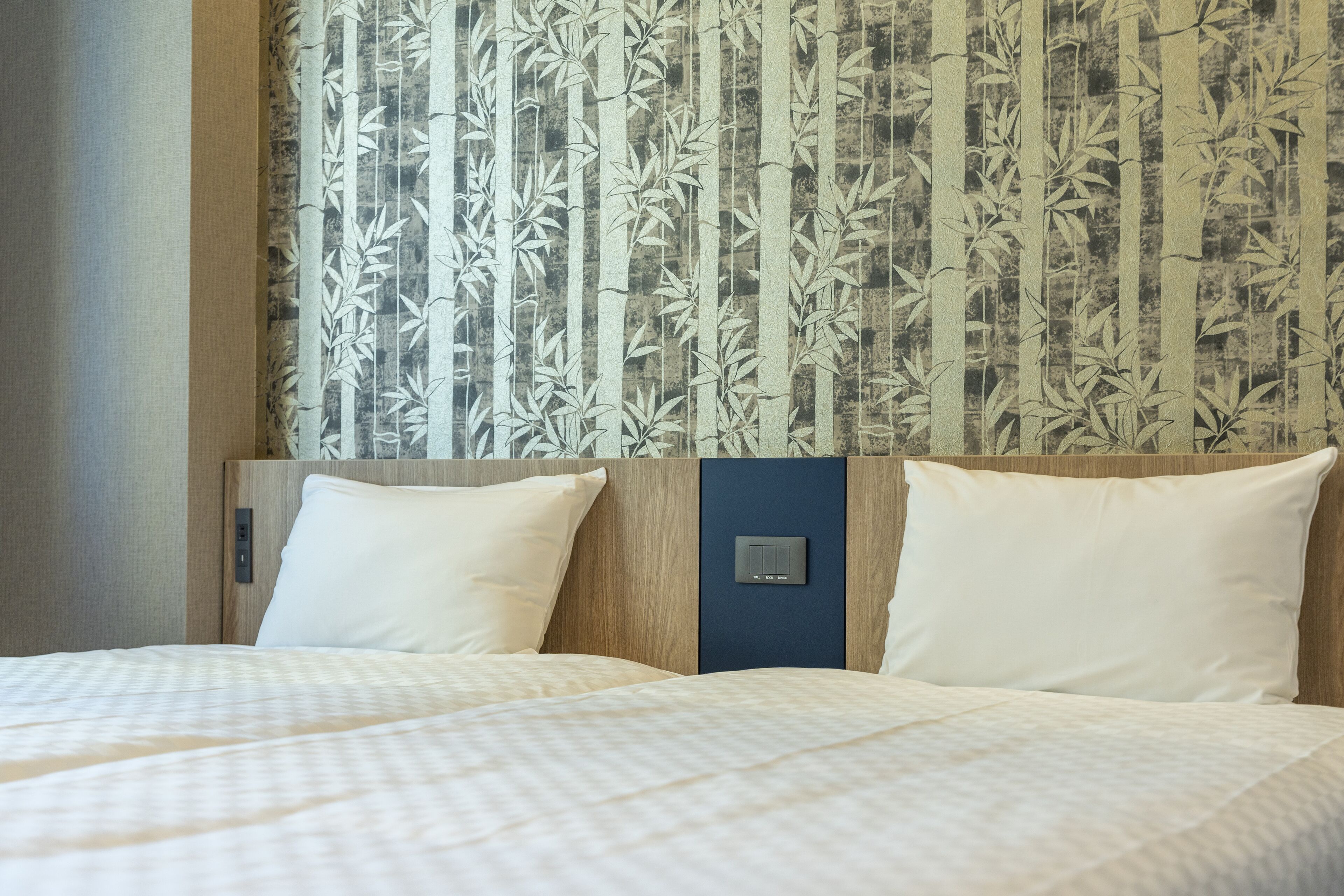 A hotel room with a bed, two pillows, a control panel, and a wall with a bamboo pattern.