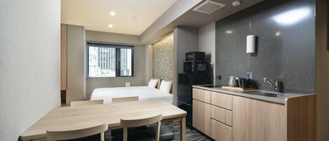 A compact hotel room with a kitchenette, a dining area, and a bed.
