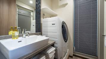 A modern bathroom with a large sink, a built-in washing machine, and a window with blinds.