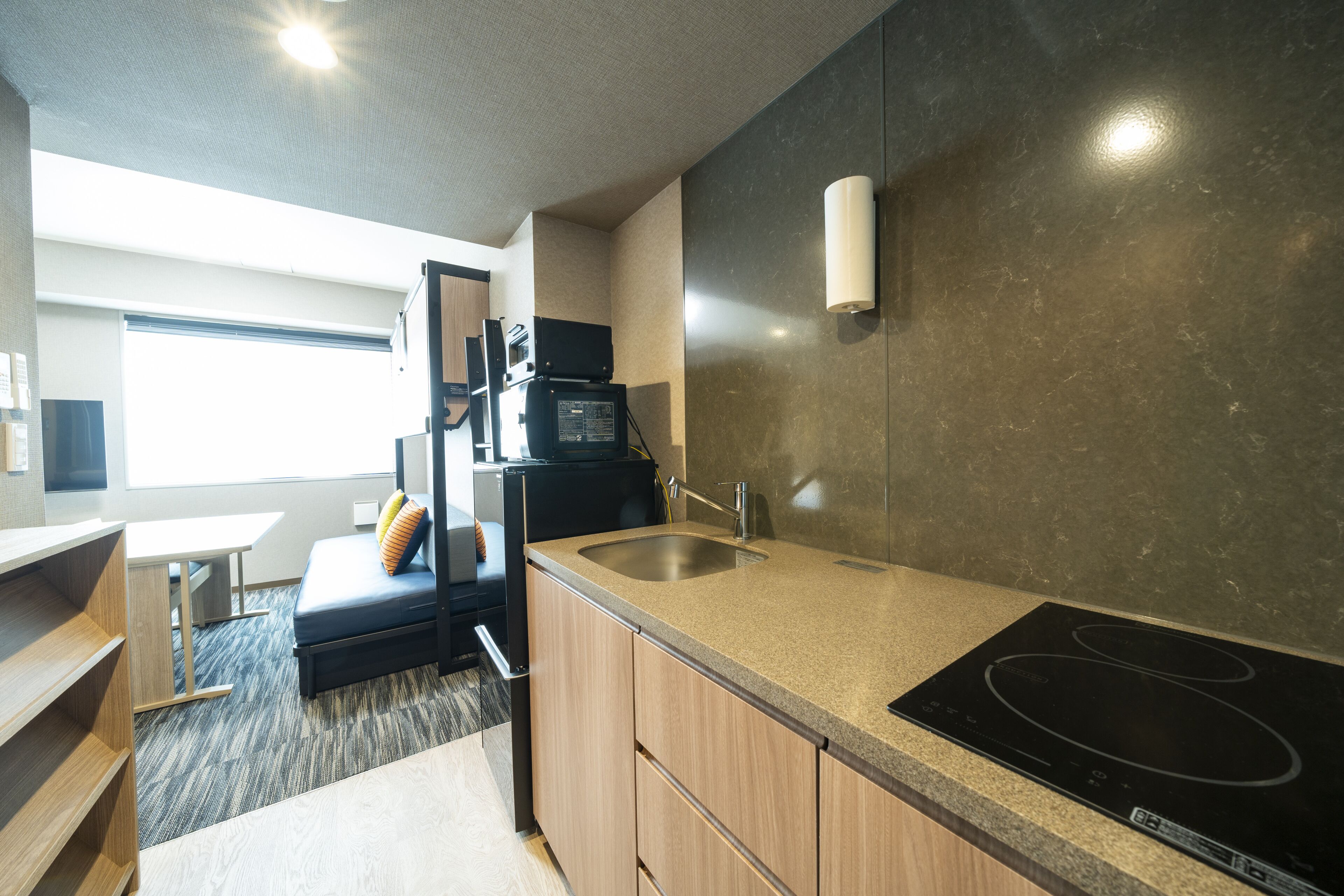 A modern kitchen with a built-in stove, a sink, and a microwave. There is a seating area with a bench and cushions.