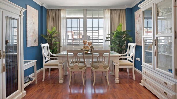 Uma área de refeições com mesa e cadeiras, uma janela com cortinas e um armário com portas de vidro.