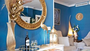 Quarto com parede azul, mesa consola branca, espelho com moldura dourada, vaso decorativo, garrafa de vinho e castiçal.