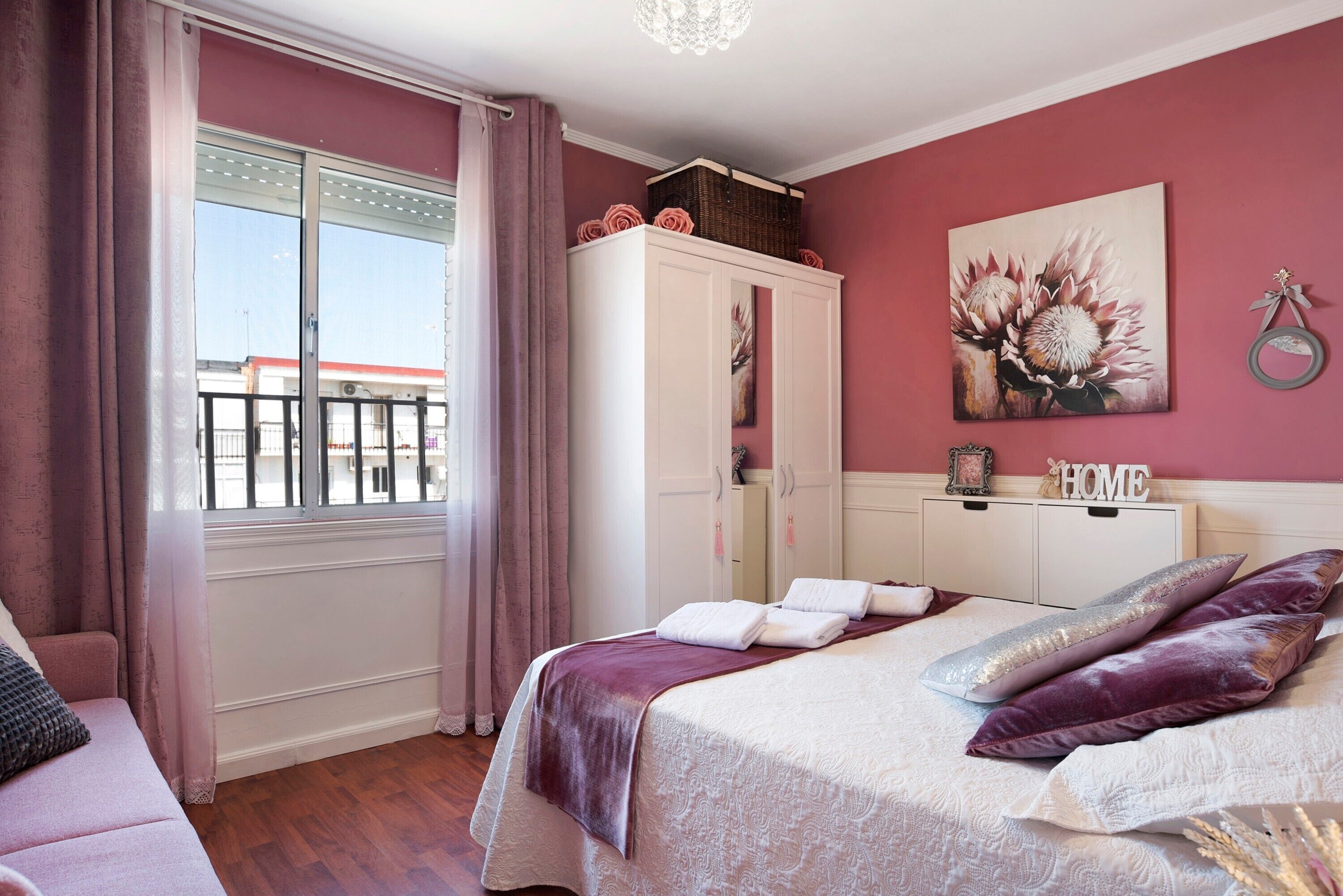 Une chambre à coucher avec un lit, une armoire, une fenêtre avec des rideaux et un mur orné d’un tableau.