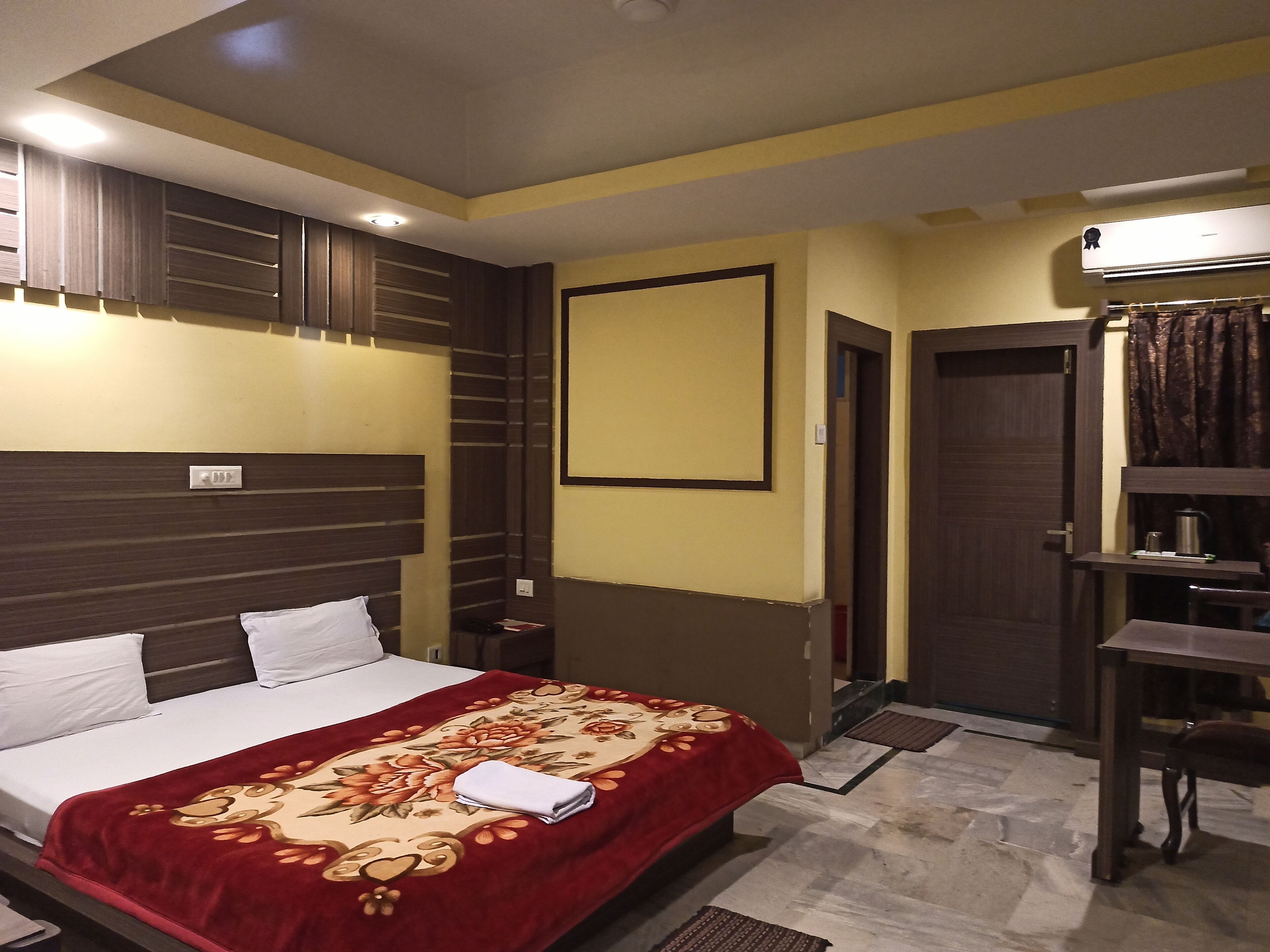 Une chambre d’hôtel comprenant un lit, une table de chevet, une commode, un climatiseur fixé au mur et une porte donnant sur une autre pièce.