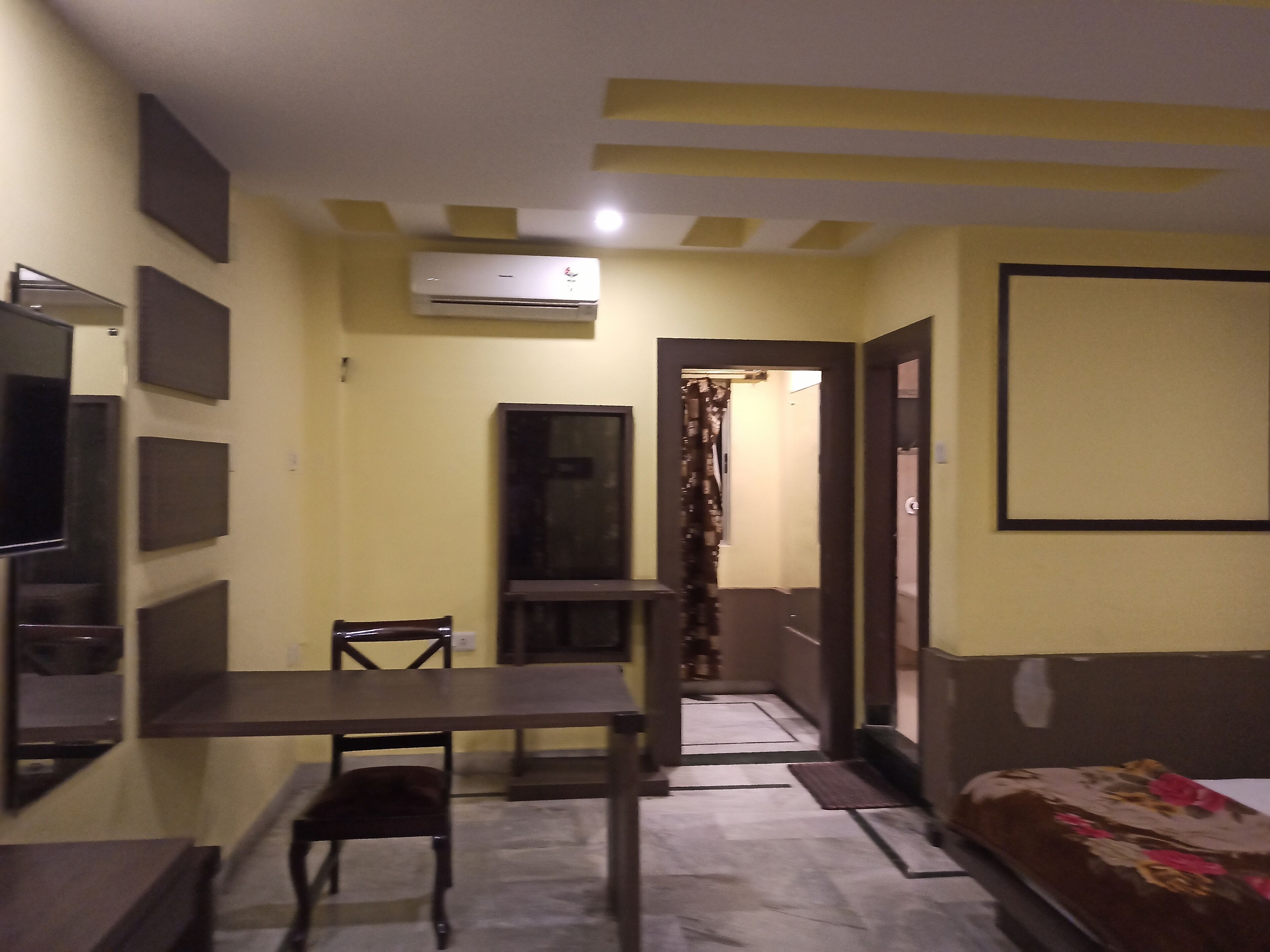 A compact hotel room with a bed, a desk, a chair, and an air conditioning unit.