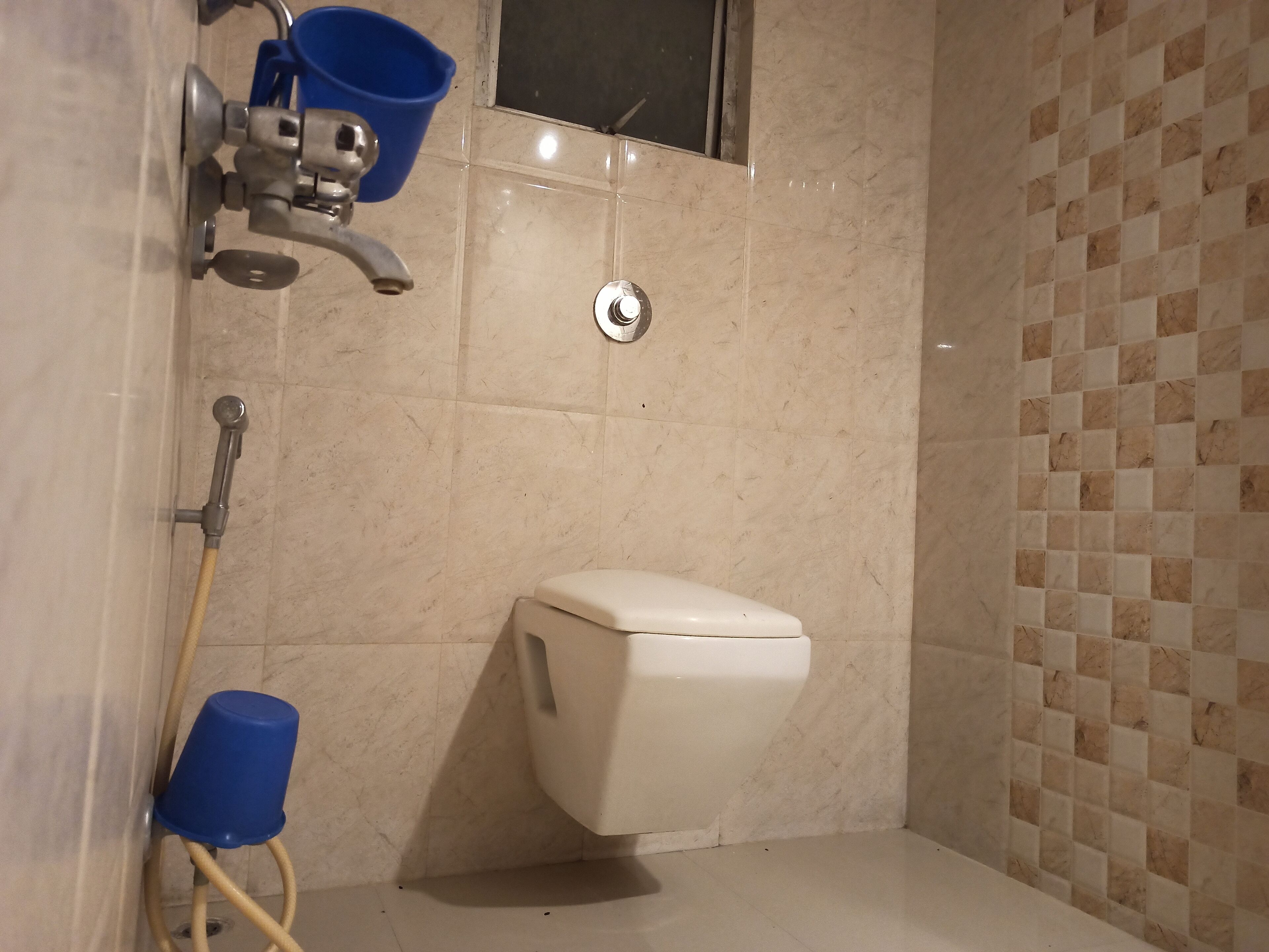 Un baño con un inodoro, un cabezal de ducha y un cubo azul.