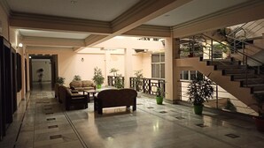A spacious lobby with a marble floor, a sofa, a coffee table, and potted plants. A staircase with a metal railing is visible on the right. - Hotel Centre Point (Tinsukia)