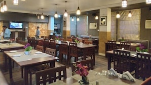 A restaurant with multiple dining tables and chairs, hanging pendant lights, and a television on the wall. - Hotel Centre Point (Tinsukia)