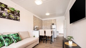 Uma sala de estar moderna com um sofá, uma área de jantar com cadeiras, uma cozinha com micro-ondas e uma TV de tela plana na parede.
