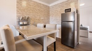Uma cozinha compacta com geladeira de aço inoxidável, micro-ondas e área de refeições com mesa e cadeiras.