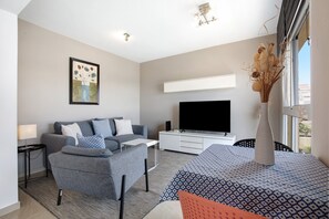 Una sala de estar moderna con un sofá, un televisor de pantalla plana, un armario blanco y un florero con plantas secas.