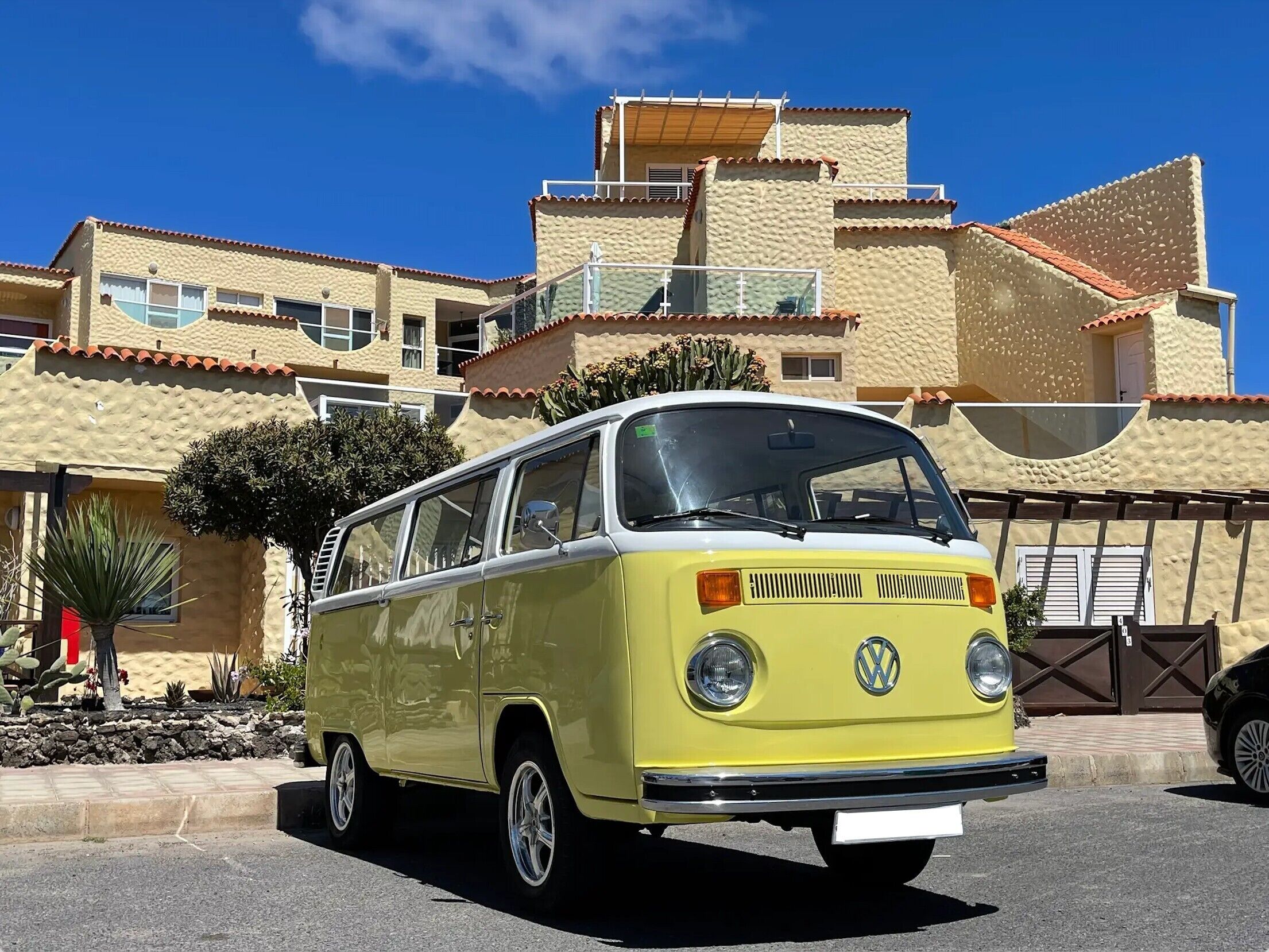 A yellow Volkswagen van parked in front of a building with multiple balconies and a tiled roof.