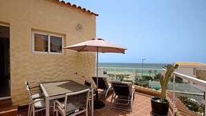 Ein Balkon mit Tisch, Stühlen, einer Topfpflanze und Blick auf den Strand.