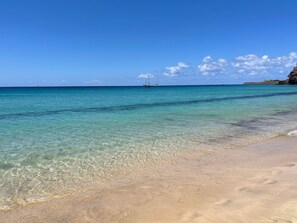 A beach with clear turquoise water, a sandy shore, and a distant sailboat.