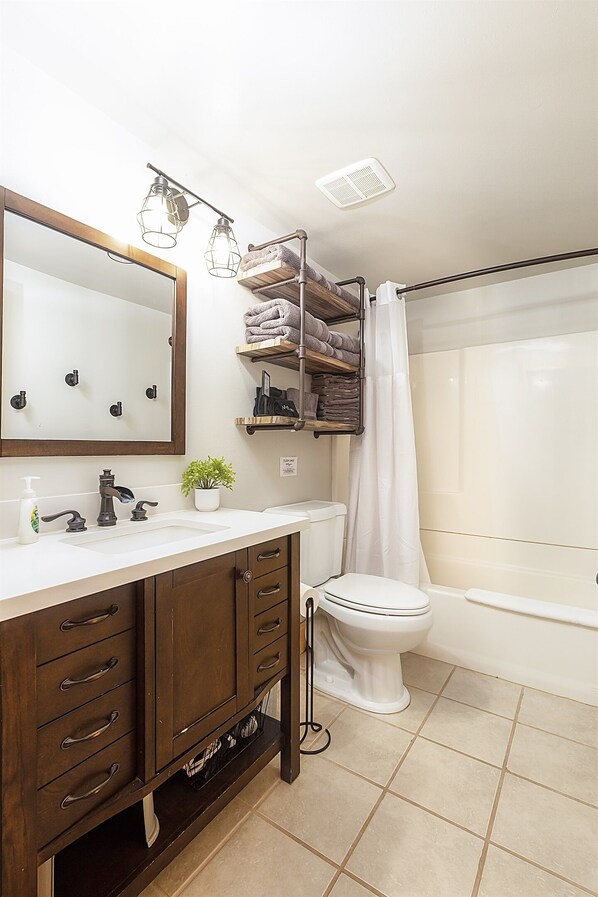 Un baño con un lavamanos blanco, un mueble de madera oscura, un espejo, un inodoro y una zona de ducha.