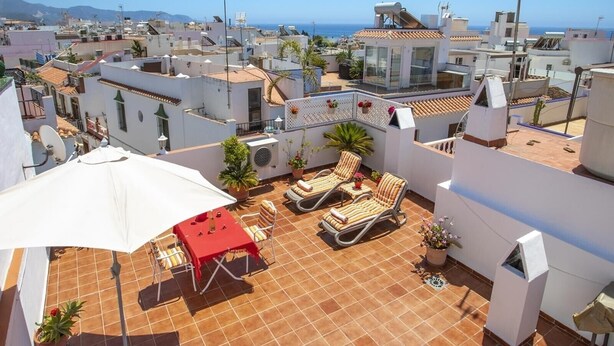 Une terrasse sur le toit, avec une table, des chaises et un grand parasol.