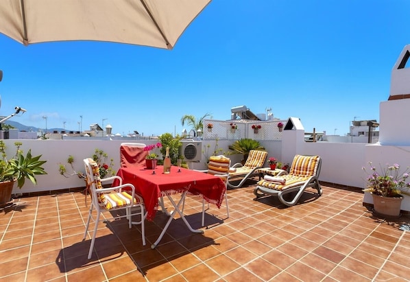 A rooftop terrace with a table and chairs, potted plants, and a view of the cityscape.