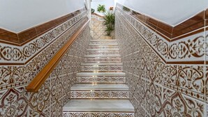 Un escalier orné de motifs complexes en carreaux, une main courante en bois et un pot de fleurs placé en haut.