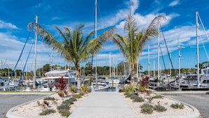 A marina with boats docked, a central walkway, and palm trees.