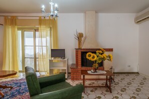 Un salón con un sillón verde, una chimenea decorada con girasoles, un televisor sobre un mueble bajo y un suelo estampado.
