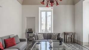 Uma sala de estar com um sofá cinzento, uma mesa de centro com objetos decorativos, um candelabro e um chão estampado.
