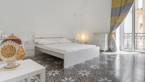 Quarto com cama branca, mesa de cabeceira, abajur e uma tigela decorativa.
