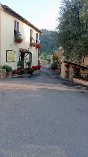 Una calle estrecha flanqueada por edificios, algunos con macetas de flores y un letrero.