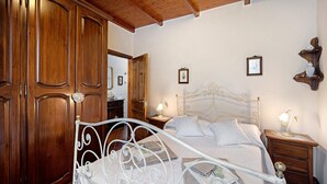 A bedroom with a metal bed frame, wooden wardrobe, bedside tables with lamps, and framed pictures on the wall.