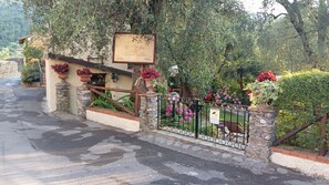 Ein rustikales Steinhaus mit einem hölzernen Schild, einem Metallgitter und einem Garten mit verschiedenen Pflanzen und Blumen.