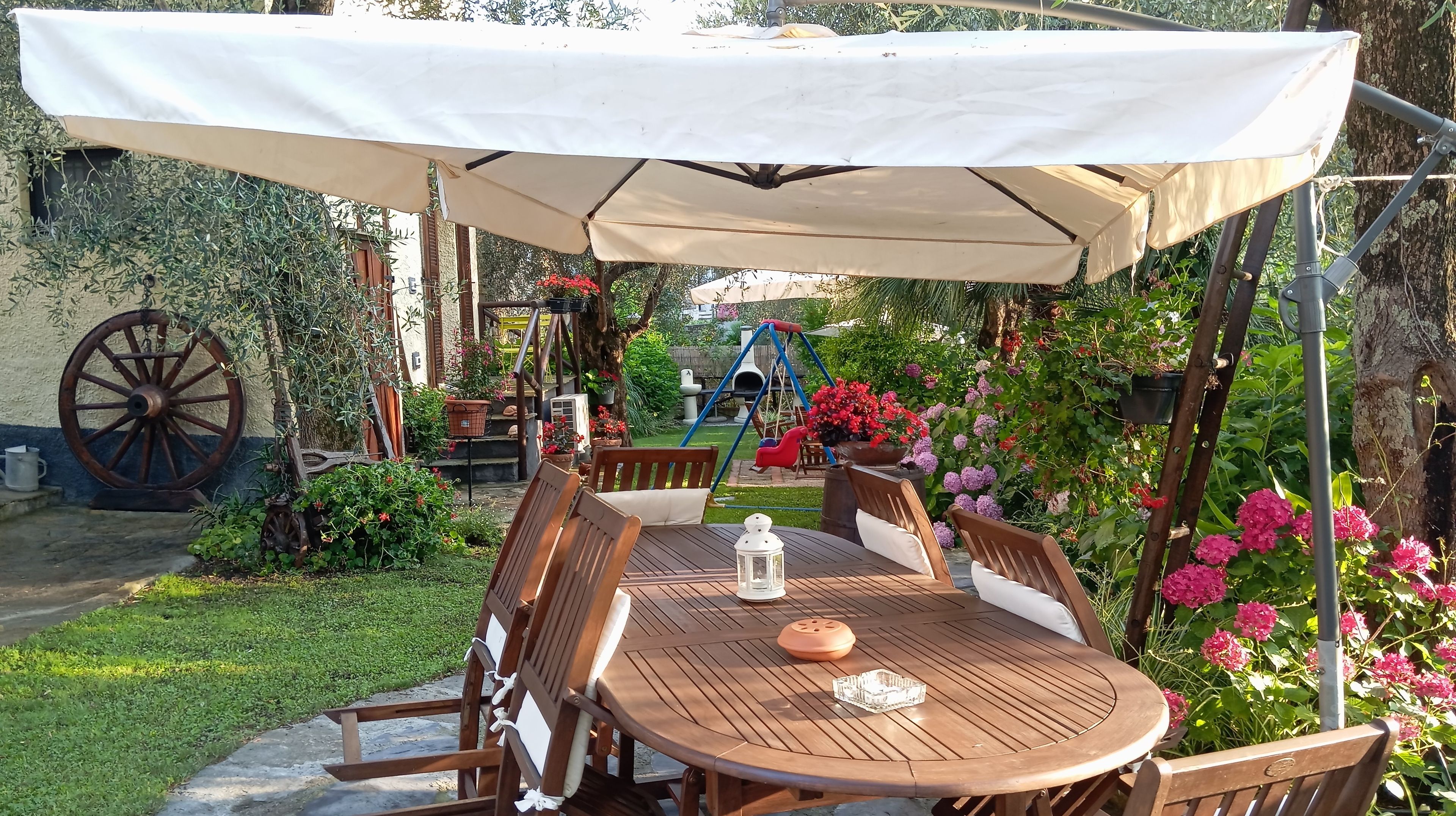 Una mesa de madera con sillas y un paraguas blanco en un jardín.