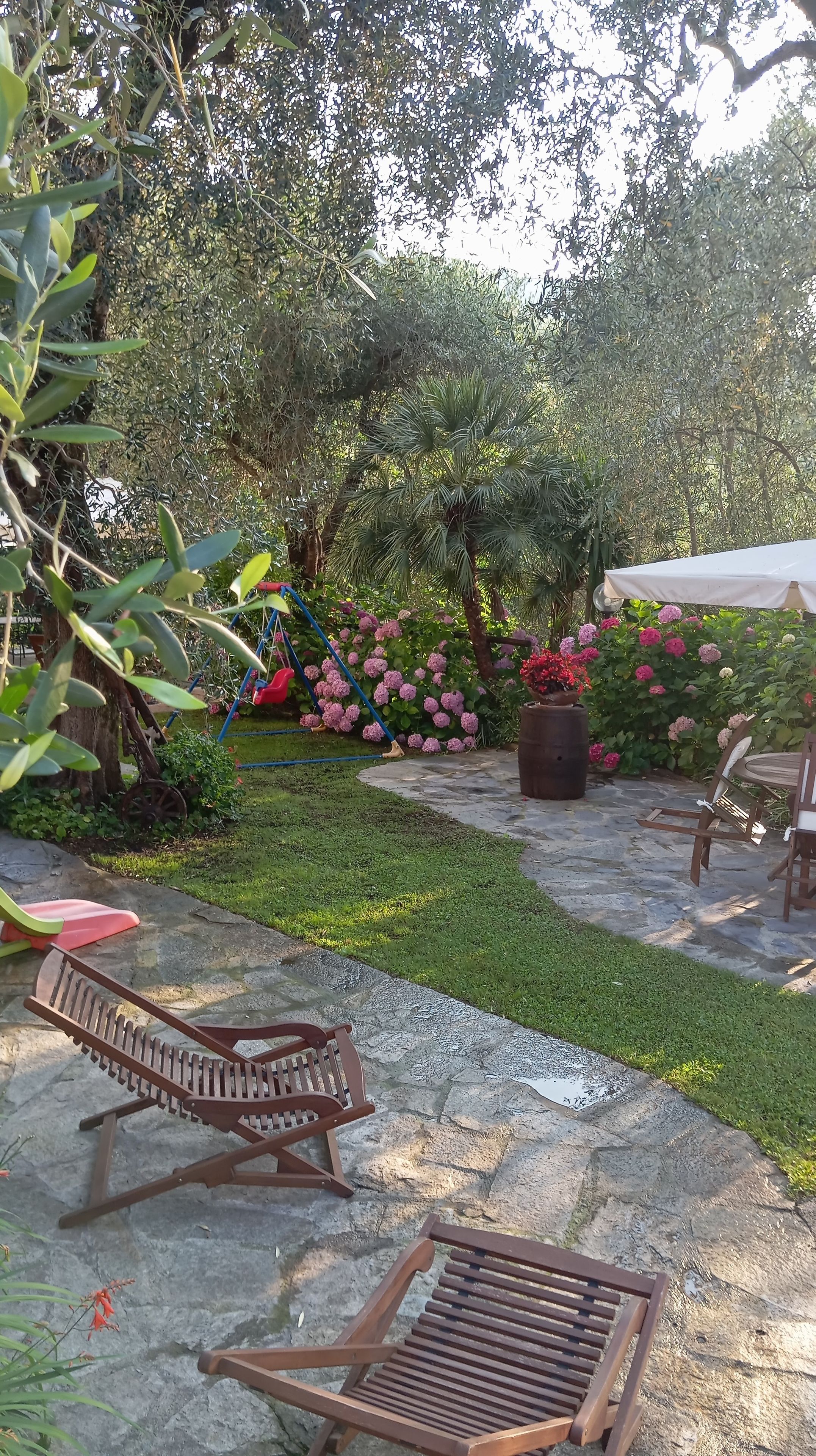 Eine Terrasse mit einer Holzbank, einer Schaukel und einem Garten mit Hortensien.