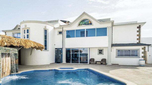 A two-story building with a swimming pool, a thatched roof structure, and a large window with a stained glass design.