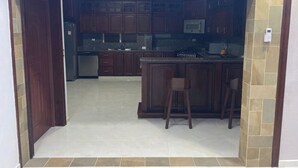 A kitchen with dark wooden cabinets, a central island with stools, and a tiled backsplash.