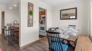 Une cuisine moderne avec des meubles en bois, un four à micro-ondes et un coin repas comprenant une table en bois dressée pour quatre personnes.