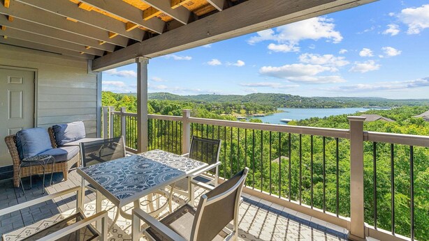 Un balcon abrité, doté d’une table et de chaises, qui offre une vue sur un lac et des collines boisées.