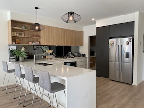 Eine moderne Küche mit Kochinsel, Barhocker, Pendelleuchten und einem Edelstahl-Kühlschrank.