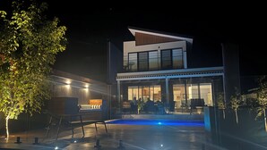 Ett modernt hus i två våningar med en swimmingpool, utomhusmöbler och en väl upplyst uteplats.