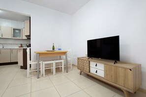 A modern kitchen with white cabinets, a wooden dining table, and a TV on a wooden cabinet.