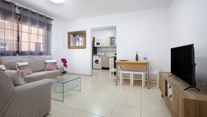 Sala de estar com sofá, mesa de centro, TV e cozinha ao fundo.