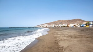 Uma praia com vista clara para o oceano, margem arenosa e uma cidade ao fundo.