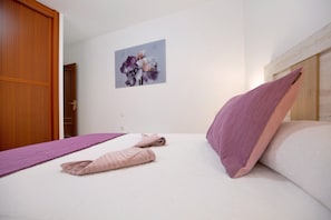 A hotel room with a bed, a wooden wardrobe, a wall-mounted picture, and a purple bedspread.